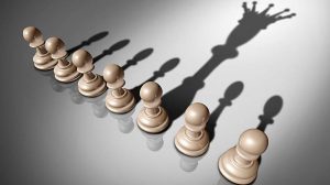 Fila de peones de ajedrez proyectando una sombra que forma la silueta de una reina, simbolizando transformación o liderazgo potencial.