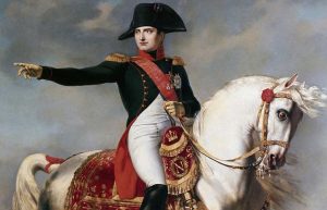 Napoleón Bonaparte montando un caballo blanco, vestido con uniforme militar negro con detalles rojos y dorados, señalando con el brazo derecho hacia adelante.