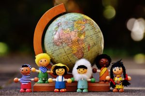 Globo terráqueo rodeado de figuras infantiles representando diversidad étnica y cultural, simbolizando la población mundial y los efectos de la revolución demográfica.