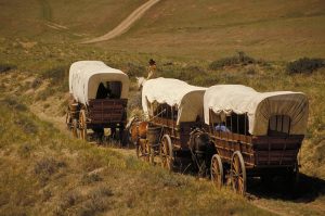 Caravana de carretas cubiertas tiradas por caballos avanzando por un sendero rural, representando migración o expansión territorial.