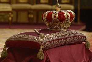 Corona y cetro reales sobre un cojín bordado en un entorno ceremonial, símbolo del poder absoluto de la monarquía