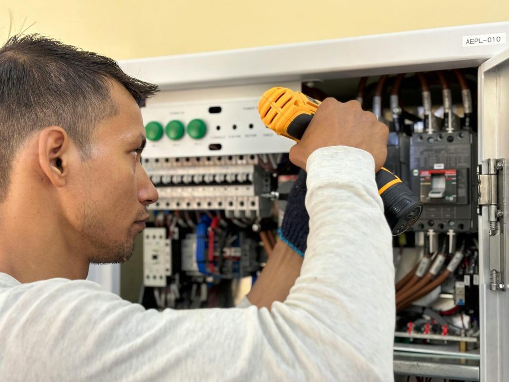 Técnico electricista revisando un cuadro eléctrico abierto, utilizando una linterna para inspeccionar el cableado y los componentes de la instalación.