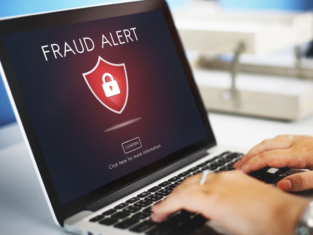 Pantalla de un ordenador portátil mostrando un aviso de “Fraud Alert” con un icono de candado, mientras una persona escribe en el teclado.