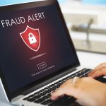 Pantalla de un ordenador portátil mostrando un aviso de “Fraud Alert” con un icono de candado, mientras una persona escribe en el teclado.