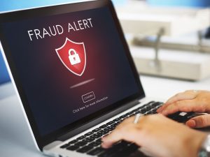 Pantalla de un ordenador portátil mostrando un aviso de “Fraud Alert” con un icono de candado, mientras una persona escribe en el teclado.
