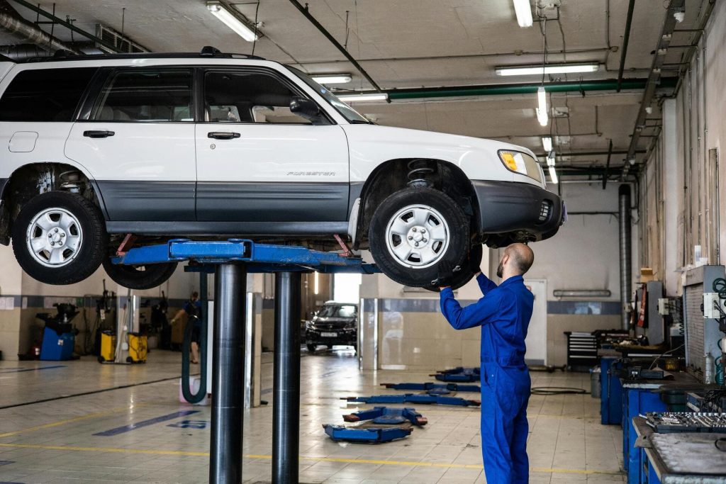 Mecánico en un taller inspeccionando un coche elevado en un elevador hidráulico, revisando la rueda y la parte inferior del vehículo.