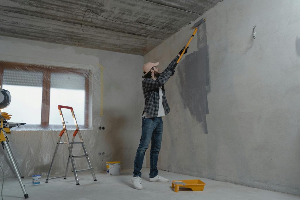 Persona pintando una pared interior con rodillo extensible durante un trabajo de bricolaje y renovación del hogar.