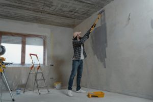 Persona pintando una pared interior con rodillo extensible durante un trabajo de bricolaje y renovación del hogar.