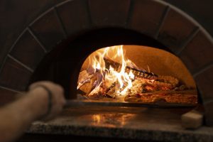 Interior de horno de leña con fuego encendido y troncos ardiendo, listo para cocinar.