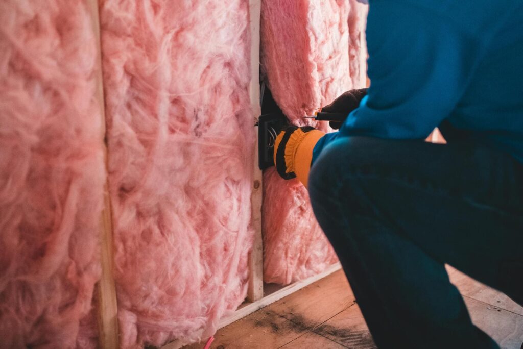 Instalador colocando aislamiento térmico de fibra de vidrio en la estructura de una pared durante una obra de construcción.