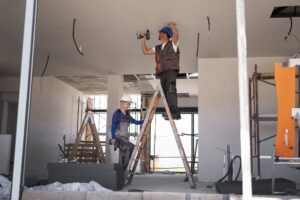 Trabajadores instalando cables eléctricos en el techo durante la reforma interior de un edificio, subidos a escaleras y utilizando herramientas eléctricas.