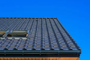 Tejado de tejas negras con ventana tipo velux bajo un cielo azul despejado.