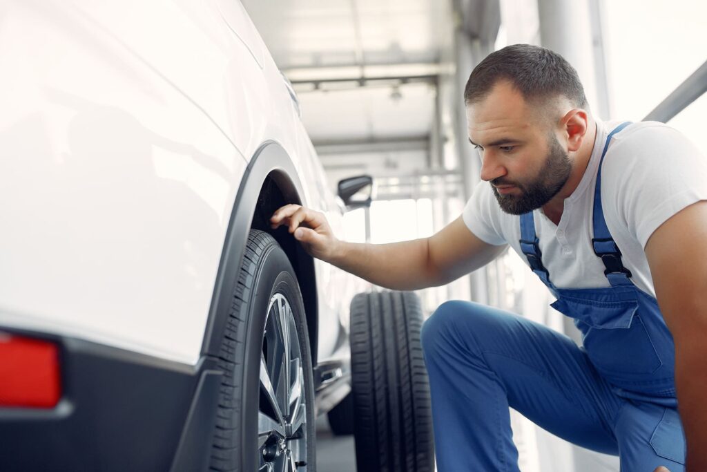 Mecánico revisando el estado del neumático de un coche en un taller, comprobando el desgaste y la seguridad de la rueda.