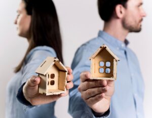 Hombre y mujer de espaldas sosteniendo pequeñas casas de madera, simbolizando divorcio, separación y reparto de bienes.