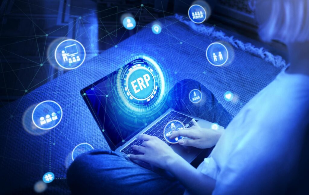Persona utilizando un ordenador portátil con interfaz digital de ERP y elementos tecnológicos conectados en un entorno azul futurista.
