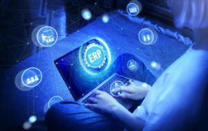 Persona utilizando un ordenador portátil con interfaz digital de ERP y elementos tecnológicos conectados en un entorno azul futurista.