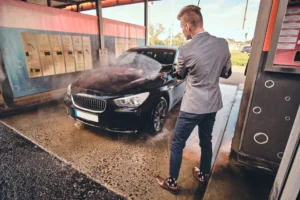Hombre lavando un coche negro con una hidrolimpiadora en un box de autolavado cubierto.