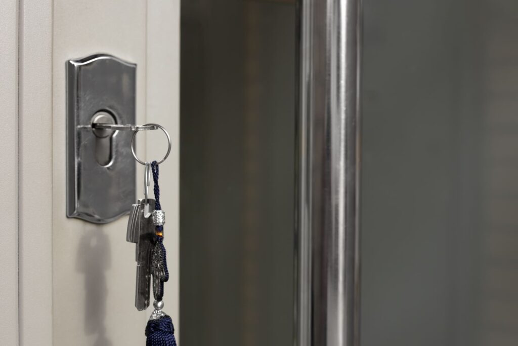 Primer plano de una llave insertada en la cerradura de una puerta, con llavero metálico colgando y fondo desenfocado en un entorno interior.
