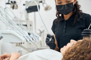 Dentista con mascarilla negra preparando instrumental para atender a una paciente en una clínica dental.