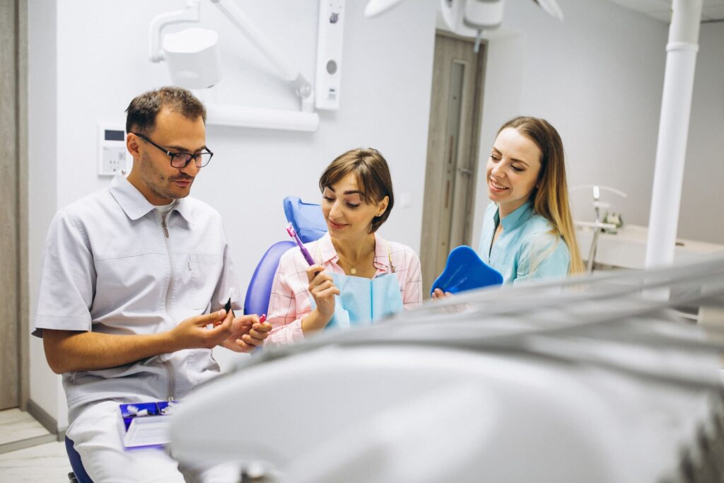 Dentista explicando un tratamiento dental a una paciente en una clínica con ayuda de una asistente.