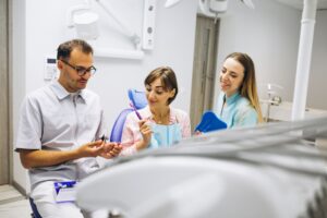 Dentista explicando un tratamiento dental a una paciente en una clínica con ayuda de una asistente.