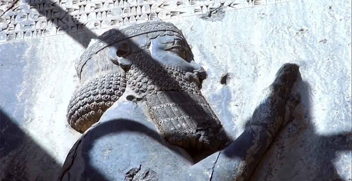 Relieve rupestre de un rey aqueménida con corona almenada bajo una inscripción cuneiforme.