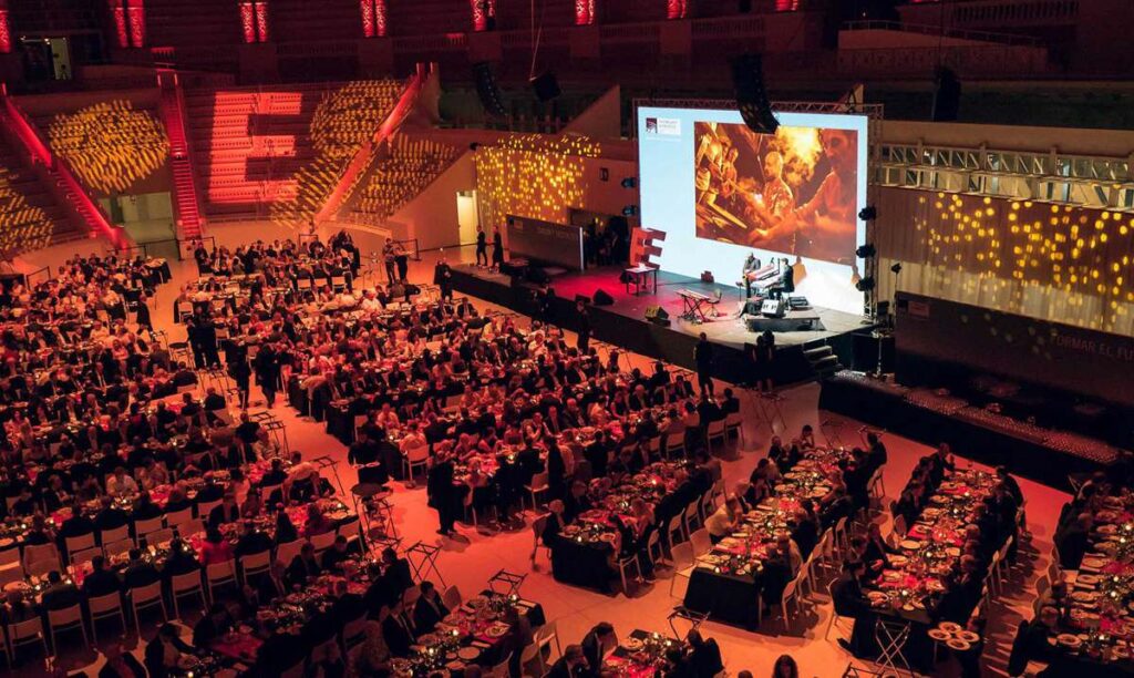 Cena de gala y evento corporativo con numerosos asistentes, escenario y gran pantalla en un recinto de Barcelona.