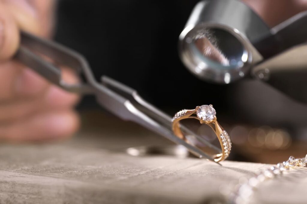 Joyero examinando con una lupa un anillo de oro con una piedra central y pequeñas piedras engastadas