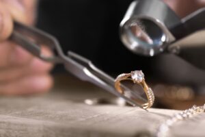 Joyero examinando con una lupa un anillo de oro con una piedra central y pequeñas piedras engastadas